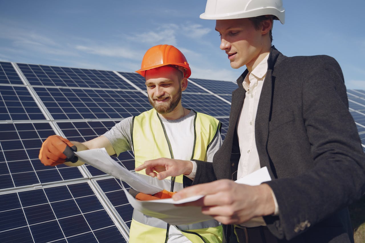 services-02 Low angle of young engineer and businessman in hardhats discussing project details against solar energy station