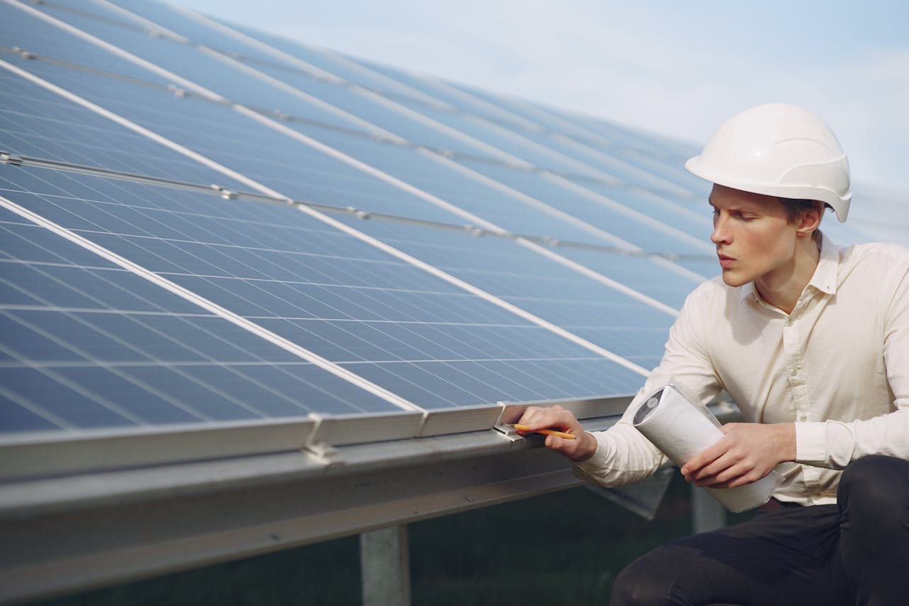 services-04 Focused young male employer in formal wear and hardhat working on solar panel station and checking details of modules